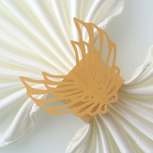 Close-up of laser-cut gold paper napkin ring with wing design and intricate hollow details