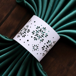 Detailed view of white laser-cut snowflake napkin ring on a dark green satin napkin