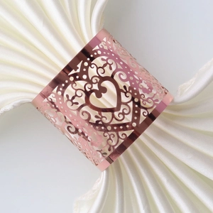Close-up of rose gold heart napkin ring with laser-cut hollow patterns on white silk
