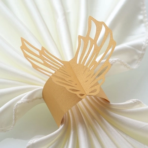 Close-up of laser-cut gold butterfly paper napkin ring on a white satin cloth