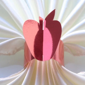 Detail of rose gold apple-shaped napkin ring with mirror finish on white satin
