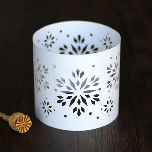 Detail of white paper napkin ring featuring laser-cut snowflake patterns on wood surface
