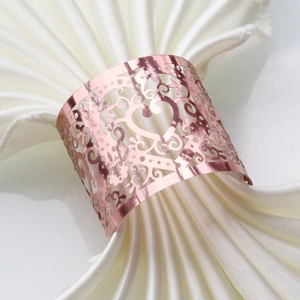 Detail of rose gold heart napkin ring with laser-cut vine patterns on white silk napkin