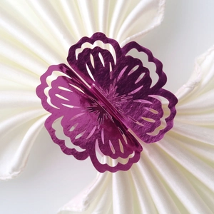 Detail of laser-cut purple flower napkin ring on white silk cloth for wedding decor