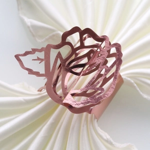 Close-up of rose gold metal napkin ring with hollow rose flower design on white cloth