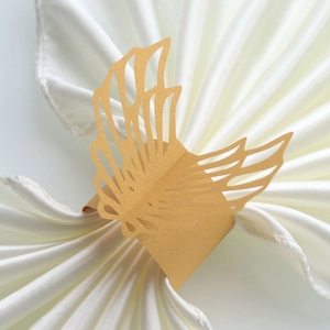 Detailed laser-cut pearl gold angel wing paper napkin ring on a white satin fabric