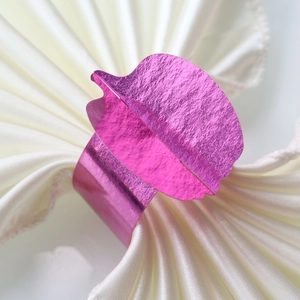 Elegant rose gold leaf-shaped napkin ring with a brushed metallic finish on white satin