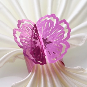 Macro shot of rose pink laser-cut butterfly napkin ring on white satin fabric