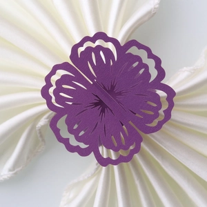 Detail showing laser-cut purple flower paper napkin ring on a white silk napkin