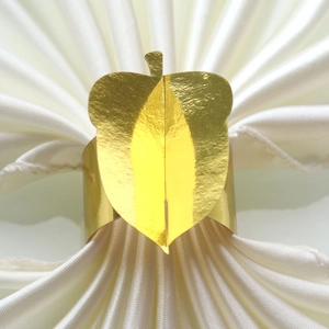Detailed close-up of a golden leaf-shaped napkin ring on a white satin fabric background