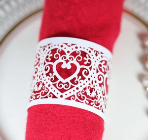 Close-up of white laser-cut heart napkin ring on red cloth for wedding table setting