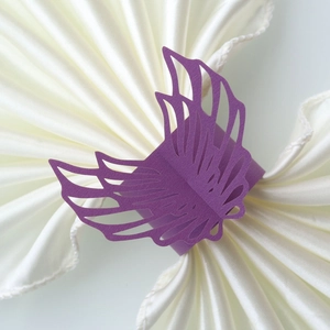 Detail of purple laser-cut wing napkin ring on white satin fabric for weddings