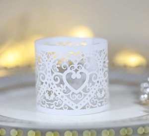 Macro detail of laser-cut heart pattern paper candle wrap on white dinner plate
