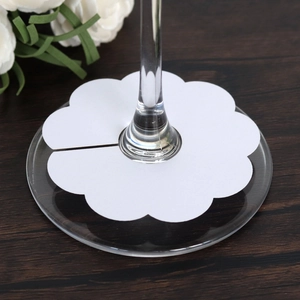 Close-up of a white flower-shaped card used as a wine glass base marker on wood table