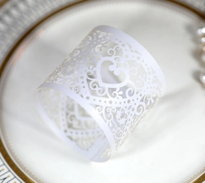 Close-up of white laser-cut paper napkin ring with heart and scroll patterns