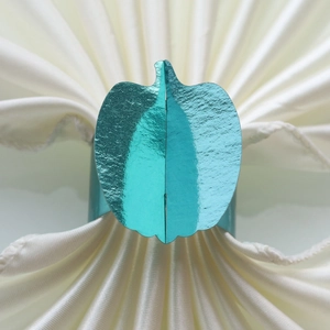 Detail view of mirror teal pumpkin napkin ring on a fan-folded white fabric background