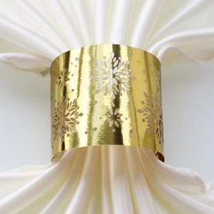 Close-up of golden snowflake napkin ring with hollow design on white satin fabric