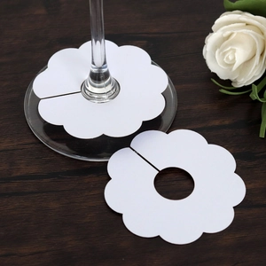 Close-up of white flower-shaped wine glass name cards on dark wood table