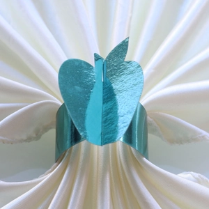 Teal heart-shaped napkin ring with metallic luster on white satin cloth for table decor