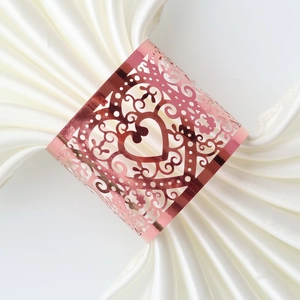 Detail of rose gold hollow heart napkin ring on white silk cloth with elegant patterns