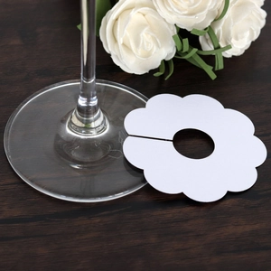 Close-up of white flower-shaped wine glass place cards on a dark wooden table background