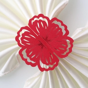 Detailed laser-cut red floral paper napkin ring on a white silk fabric background