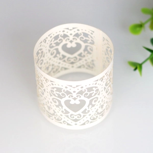 Detailed laser-cut white paper napkin ring featuring intricate hollow heart and scroll patterns
