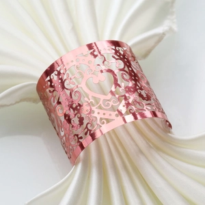 Detail of rose gold heart pattern napkin ring on white satin fabric with laser cutout