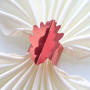 Gros plan du rond de serviette en forme de feuille de chêne or rose sur du satin blanc