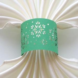 Detail of laser-cut snowflake napkin ring in mint green on white satin fabric