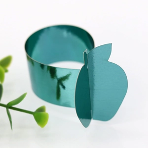 Detail showing metallic teal apple-shaped napkin ring on minimalist white surface