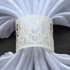 Detail showing cream laser-cut heart napkin rings on a white folded cloth napkin