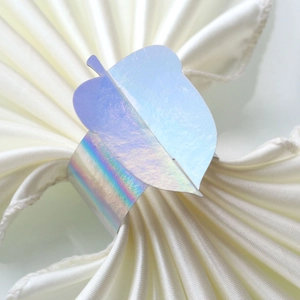 Iridescent leaf napkin ring with holographic finish on elegant white satin cloth