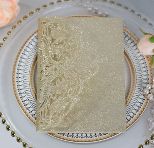 Close-up of laser-cut lace pattern on gold glitter wedding invitation card with pink rose