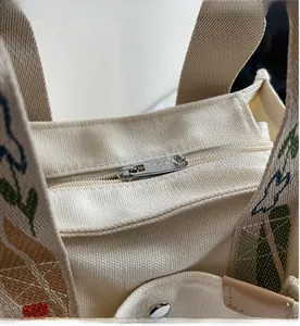 Detail of beige canvas tote featuring metal zipper with butterfly charm and floral embroidery
