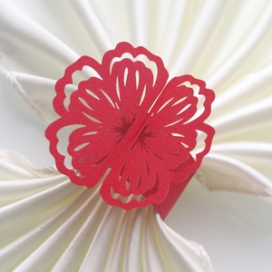Close-up of laser-cut red floral paper napkin ring on a white silk napkin