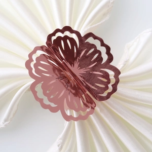 Detail showing a rose gold flower napkin ring with hollow petals on white satin cloth