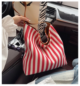 Detail of red and white striped canvas tote bag with brown leather strap in a car setting