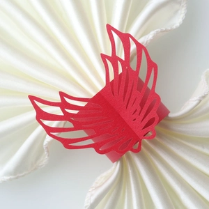 Macro view of laser-cut red butterfly paper napkin ring on a white satin napkin