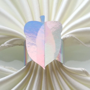 Detailed view of holographic acorn-shaped napkin ring on a white silk table napkin