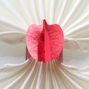 Detail showing red metallic apple-shaped napkin ring on a white folded cloth