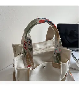 Detail of white canvas tote bag featuring floral embroidered strap and metal hardware