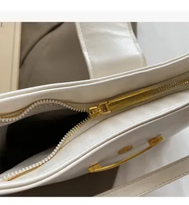 Detail of the smooth gold metal zipper and white textured faux leather on the dumpling bag
