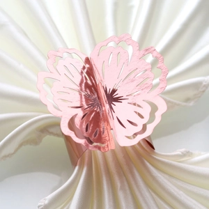 Detailed macro view of laser-cut rose gold butterfly napkin ring on white satin fabric