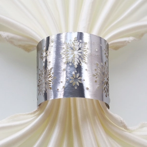 Close-up of elegant silver snowflake napkin ring with intricate cutout design on white silk