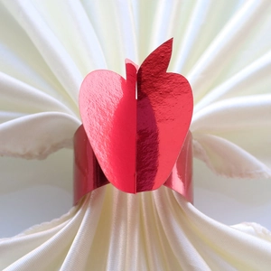 Detail of red apple napkin ring with a metallic finish on a white satin fabric background