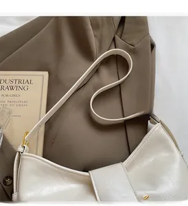 Detail of a creamy white crescent bag with wrinkled texture on a brown blazer backdrop