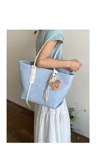 Detail of light blue tote bag with crocodile texture, cream straps and bear pendant