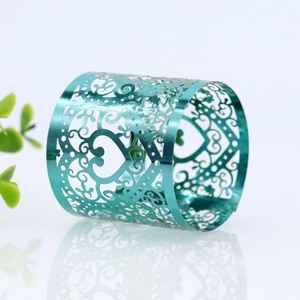 Macro shot of laser-cut heart pattern teal metal napkin ring on reflective surface
