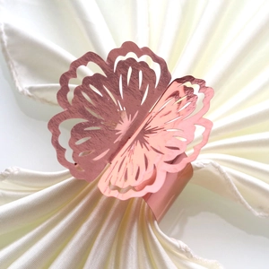 Close-up of rose gold hollow flower napkin ring on a folded silk cream napkin